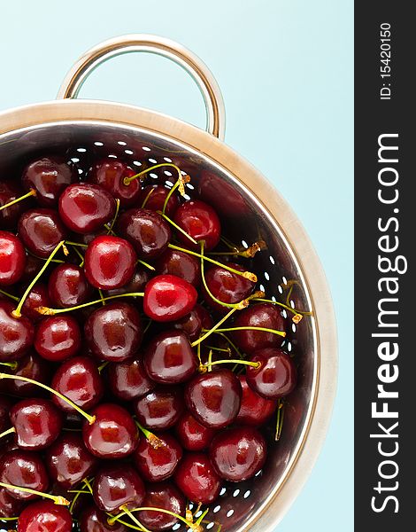 A large selection of ripe cherries in a colander with a blue background