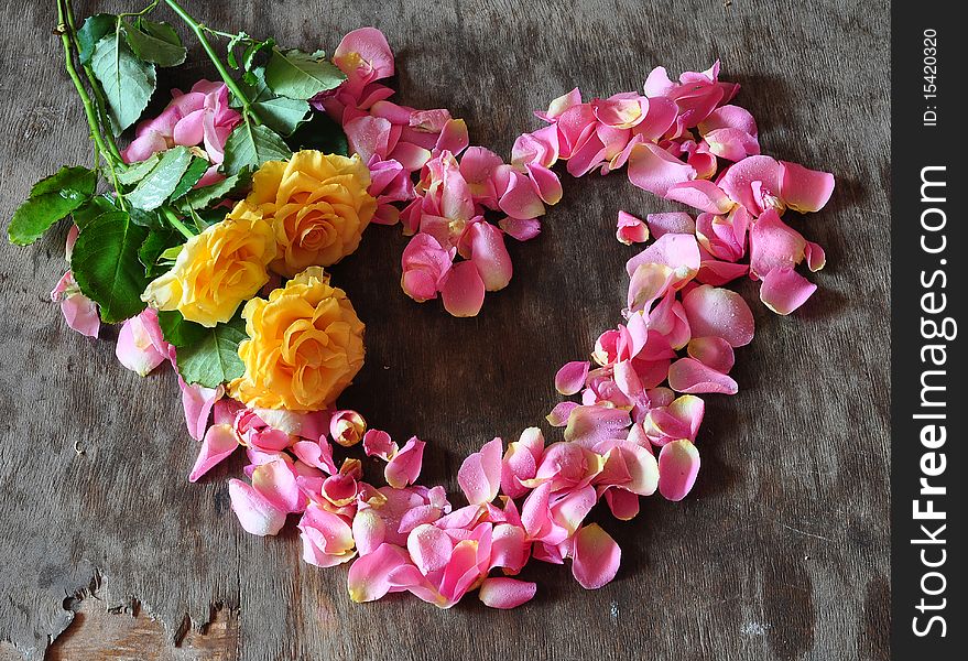 Heart from the petals of pink rose on a table, three yellow roses lie on a heart. Heart from the petals of pink rose on a table, three yellow roses lie on a heart