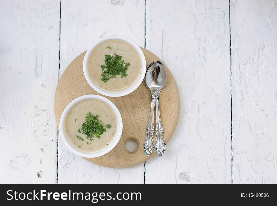 Mushroom soup with parsley in white ceramic bowl and spoon on a wooden board