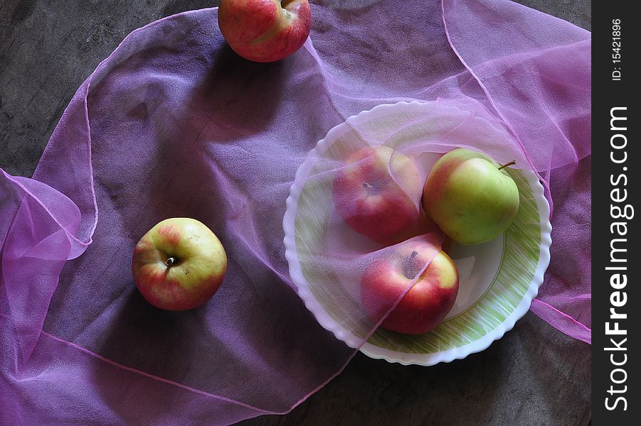 three apples lie on a dish, two apples lie alongside, fabric lies on apples. three apples lie on a dish, two apples lie alongside, fabric lies on apples