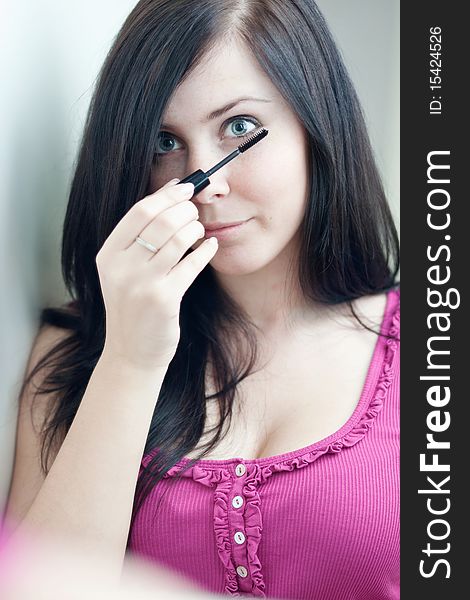 Pretty young woman applying mascara /eye shadows in front of a mirror