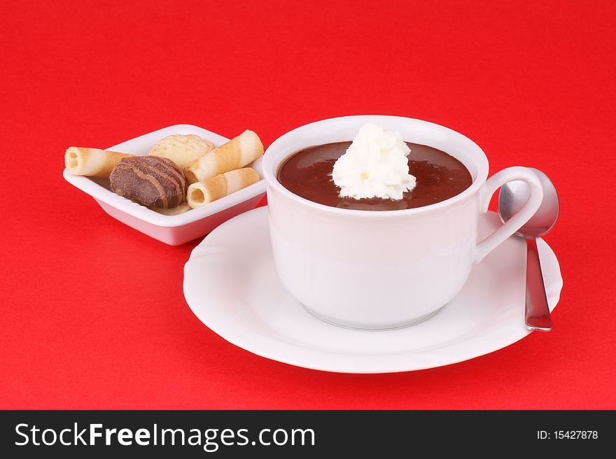 Cup of hot chocolate served with whipped cream and some cookies. Studio shot over red background. Cup of hot chocolate served with whipped cream and some cookies. Studio shot over red background.