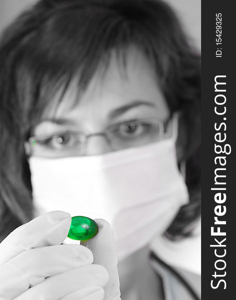 Confident female doctor holding a green pill in black and white