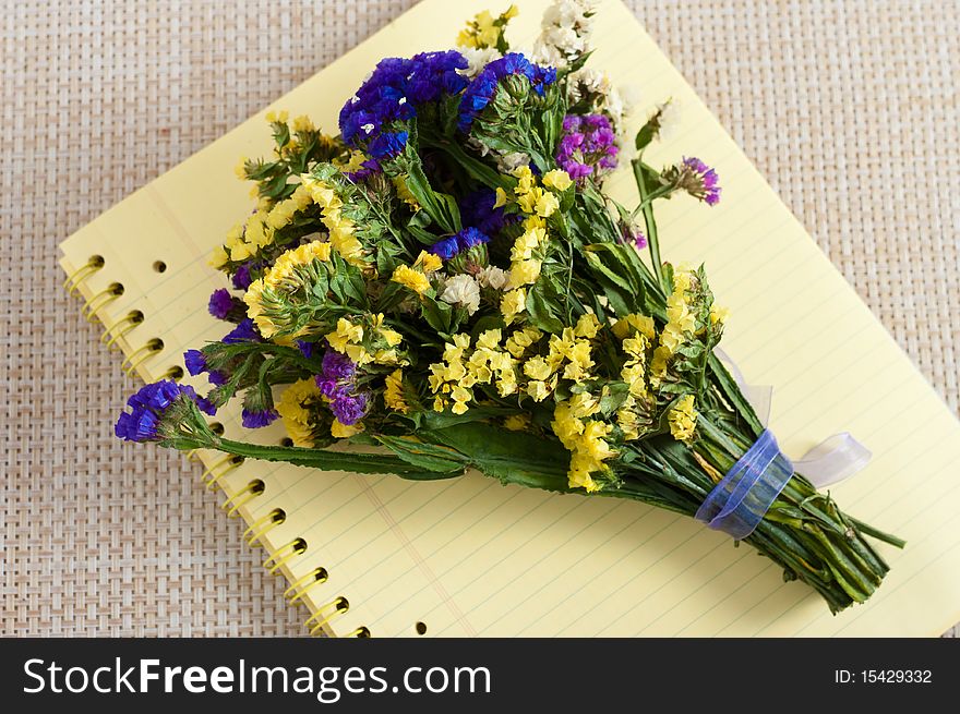 A bunch of immortelle flowers tied with violet organza ribbon set on a yellow copybook on the table. A bunch of immortelle flowers tied with violet organza ribbon set on a yellow copybook on the table