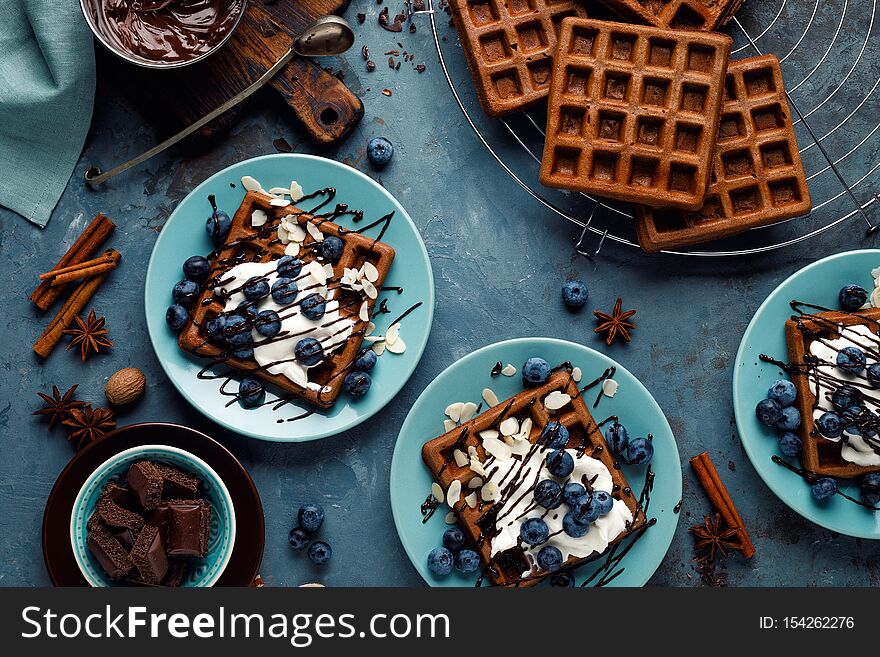 Chocolate belgian waffles with ice cream and fresh blueberry on blue background, top view