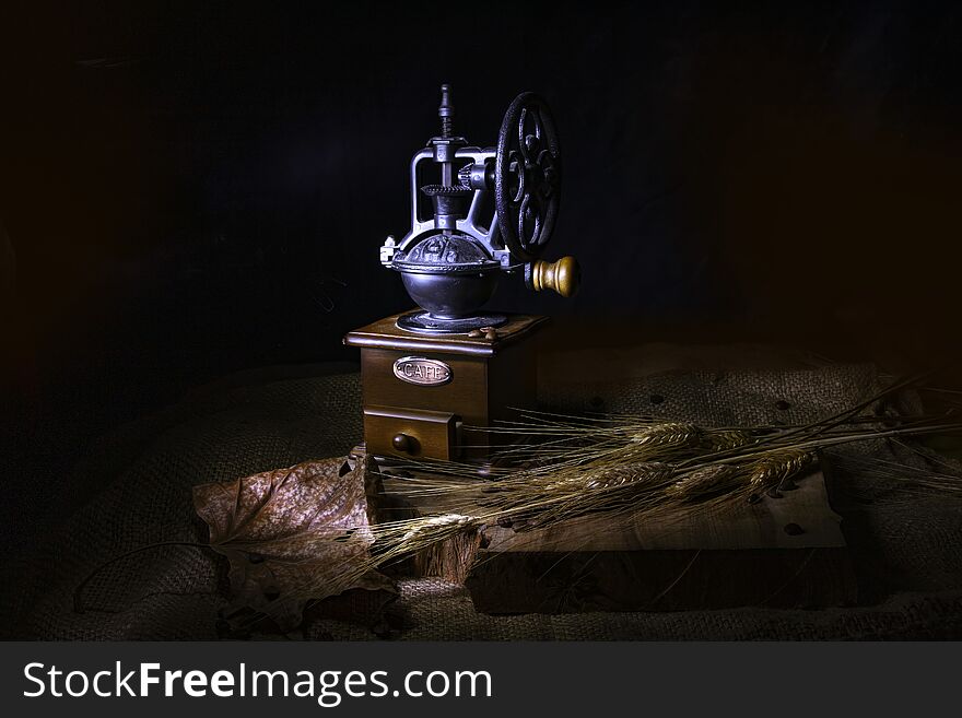 Still life on a black background. Vintage coffee grinder, dry leaves and ears of wheat on a burlap-covered wooden table