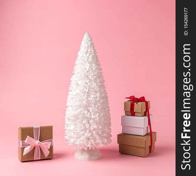 Snowy Christmas tree with gift boxes on pastel pink background. Christmas or New Year minimal concept