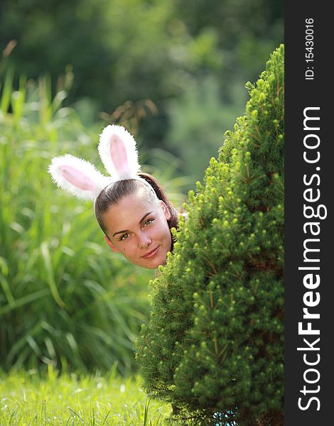 Girl with funny rabbit ears playfully peeking out behind from the tree