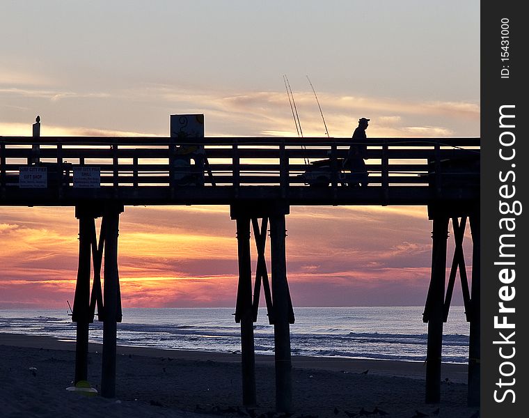 Silhouetted fisherman on pier at sunrise