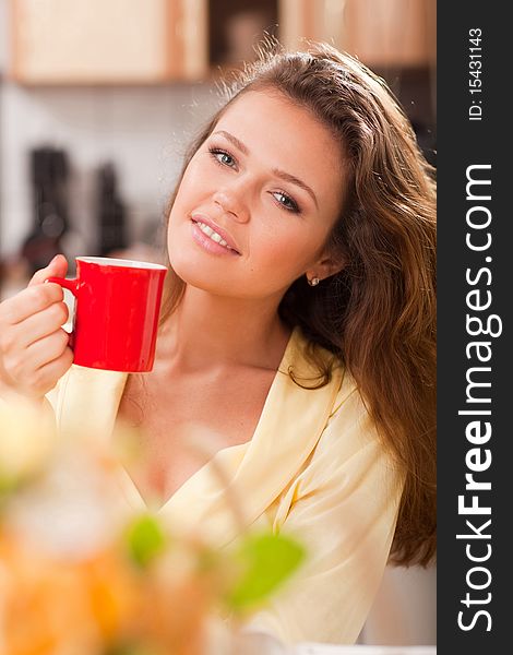 Attractive young adult with red cup of tea in the kitchen. Attractive young adult with red cup of tea in the kitchen