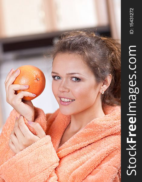 Pretty young adult in the kitchen with orange wearing bathrobe. Pretty young adult in the kitchen with orange wearing bathrobe