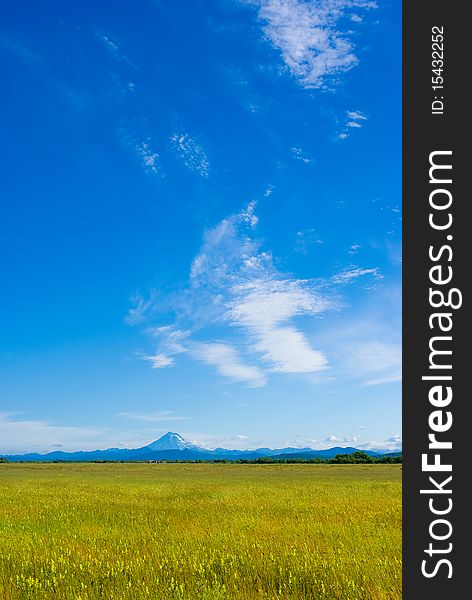 The meadow with the grass against the sky and the volcano in the distance. The meadow with the grass against the sky and the volcano in the distance