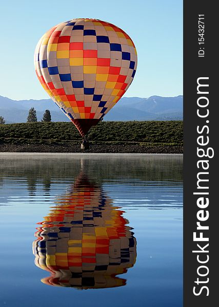 A colorful hot air balloon floats close to the surface of a glassy lake. A colorful hot air balloon floats close to the surface of a glassy lake