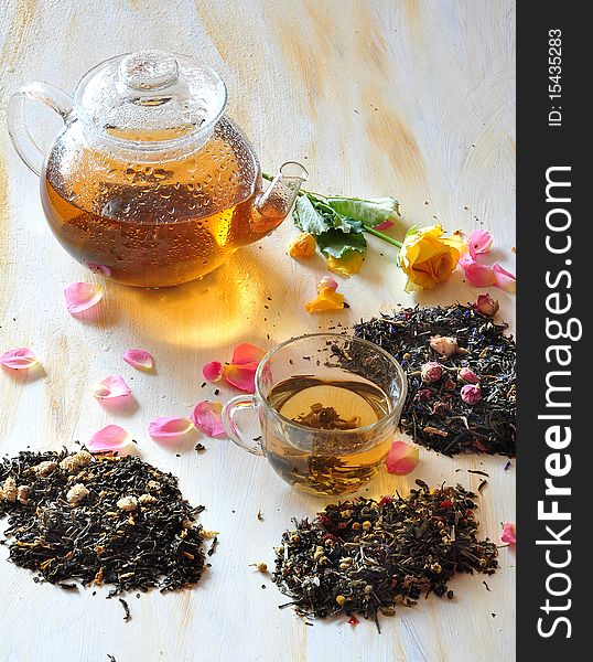 Tea is brewed in a glass tea-pot, alongside cup with tea, petals of roses and dry tea coupage. Tea is brewed in a glass tea-pot, alongside cup with tea, petals of roses and dry tea coupage