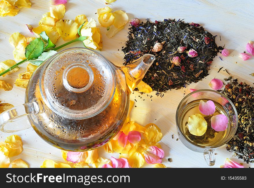 Tea is brewed in a glass tea-pot, alongside cup with tea, petals of roses and dry tea coupage. Tea is brewed in a glass tea-pot, alongside cup with tea, petals of roses and dry tea coupage