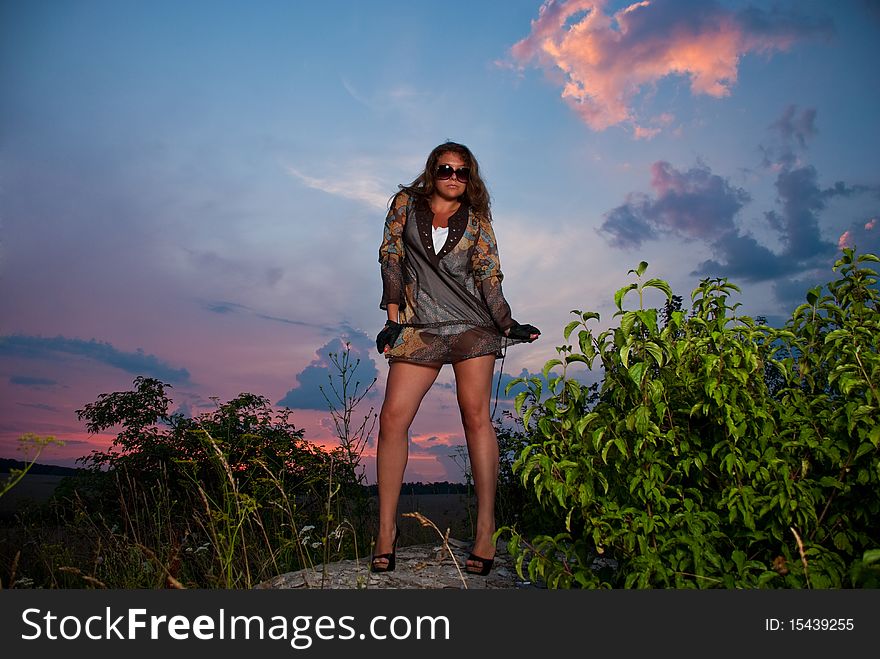 Young woman in sunglasses standing at sunset rock. Young woman in sunglasses standing at sunset rock