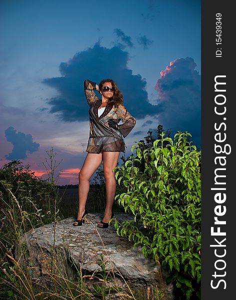 Young woman in sunglasses standing at sunset rock. Young woman in sunglasses standing at sunset rock