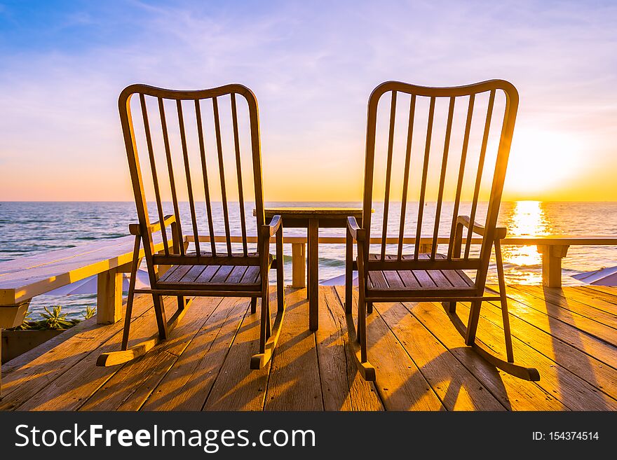 Empty wood chair and table at outdoor patio with beautiful tropical beach and sea at sunrise or sunset background for vacation and travel
