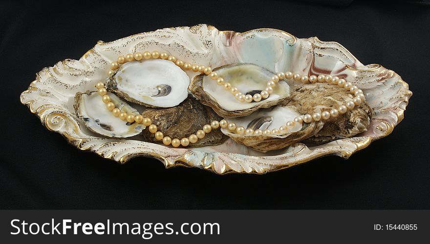 A string of pearls resting on oyster shells on a colorful plate against a black background. A string of pearls resting on oyster shells on a colorful plate against a black background