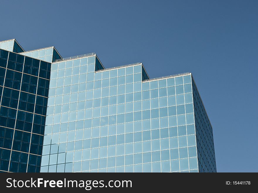 Detail of the architecture of a modern office building with reflective glass exterior windows. Clear blue sky.