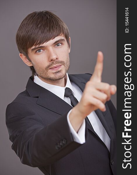 Young businessman pointing with finger on something over grey background