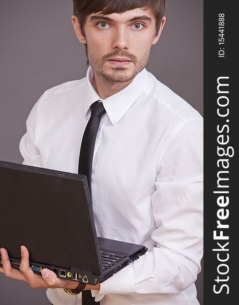 Young businessman in white shirt holding laptop computer over grey background. Young businessman in white shirt holding laptop computer over grey background