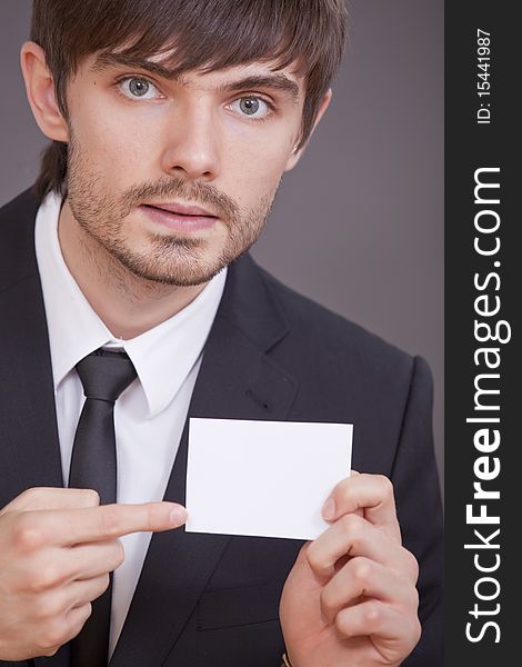 Businessman pointing with his finger on blank visit card over grey background. Businessman pointing with his finger on blank visit card over grey background