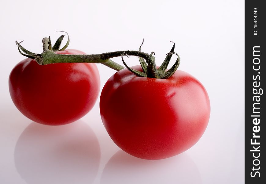 The photo shows two tomatoes over white, reflective ground. The photo shows two tomatoes over white, reflective ground