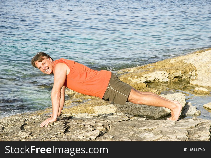Color portrait photo of a happy smiling man in his forties performing push ups on a rocky beach. Color portrait photo of a happy smiling man in his forties performing push ups on a rocky beach.