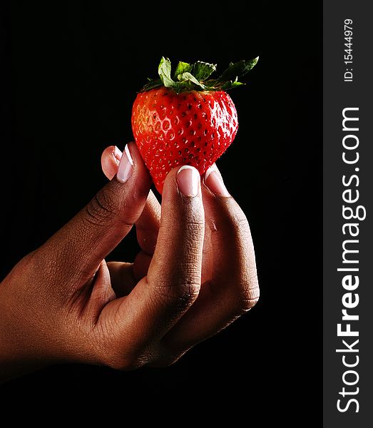 Womand holding a strawberry on a black backdround