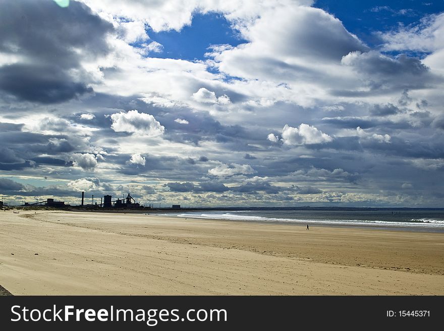 Lonely man walking on beach with industry in background and dramatic sky