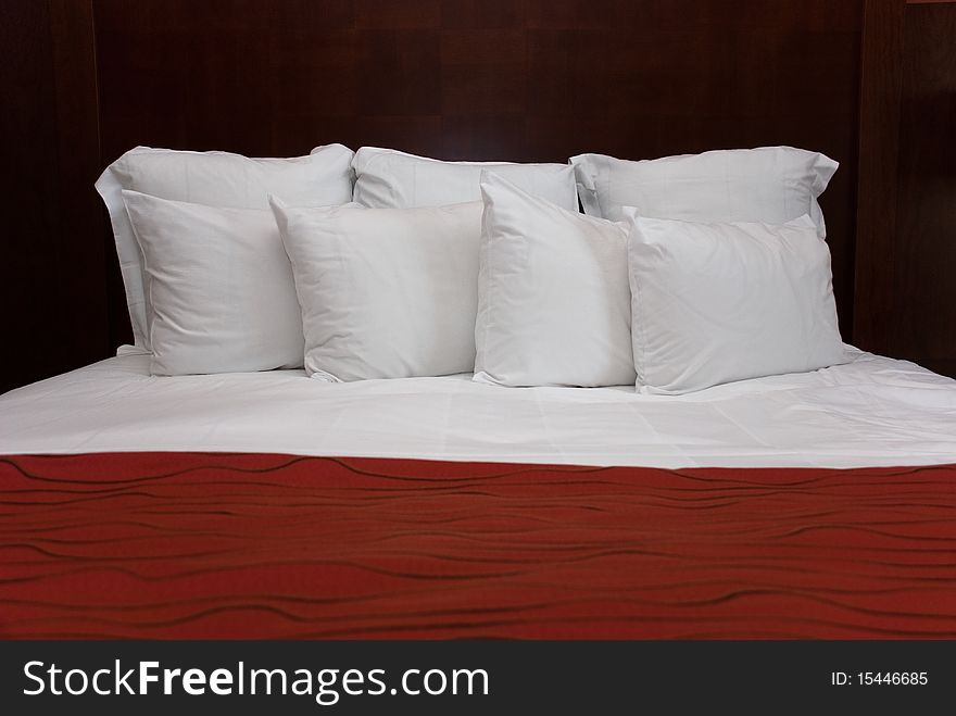 Eight white fluffy pillows on white sheets with a red bedspread against a wood headboard. Eight white fluffy pillows on white sheets with a red bedspread against a wood headboard.
