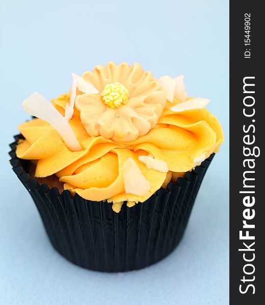 A freshly baked cup cake with orange frosting