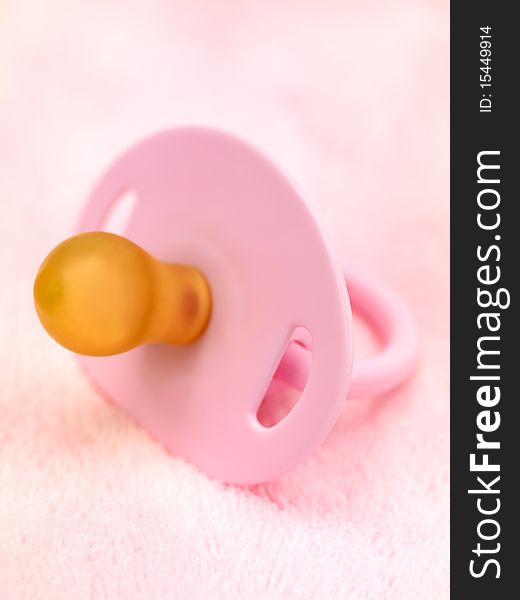 A pink pacifier isolated against a pink background