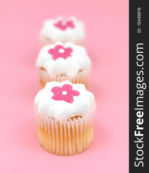 Freshly baked cup cakes with pink flowers and white frosting