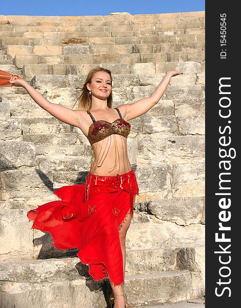 Beautiful belly dancer in red on the ancient stairs of Kourion amphitheatre in Cyprus.