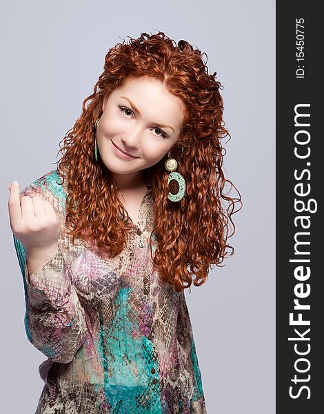 Caucasian red haired girl showing come on sign with pretty natural smile on face standing isolated on gray background