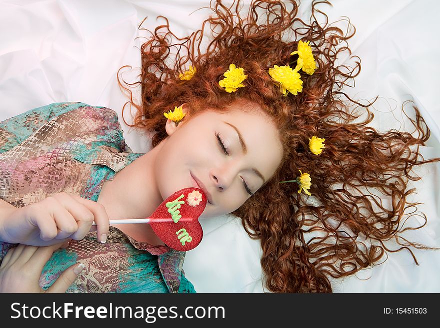 Young caucasian girl lying over white linen and hair spread over the floor with flowers on it having gentle touch of sweet candy and relaxing dreaming look. Young caucasian girl lying over white linen and hair spread over the floor with flowers on it having gentle touch of sweet candy and relaxing dreaming look