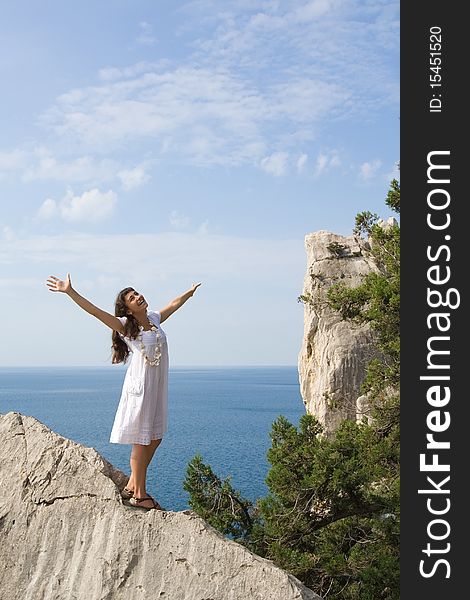 Happy young girl standing on the rocks with her hands up with the sea as a background. Happy young girl standing on the rocks with her hands up with the sea as a background