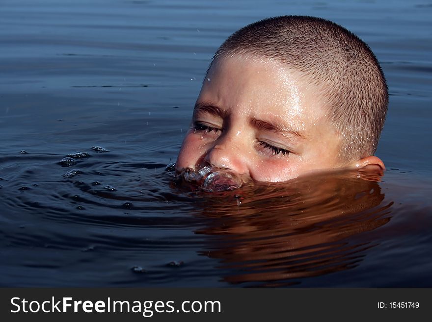 The boy frolics in a pond, starts up bubbles. Over water the top part of a head is visible, eyes are blinked