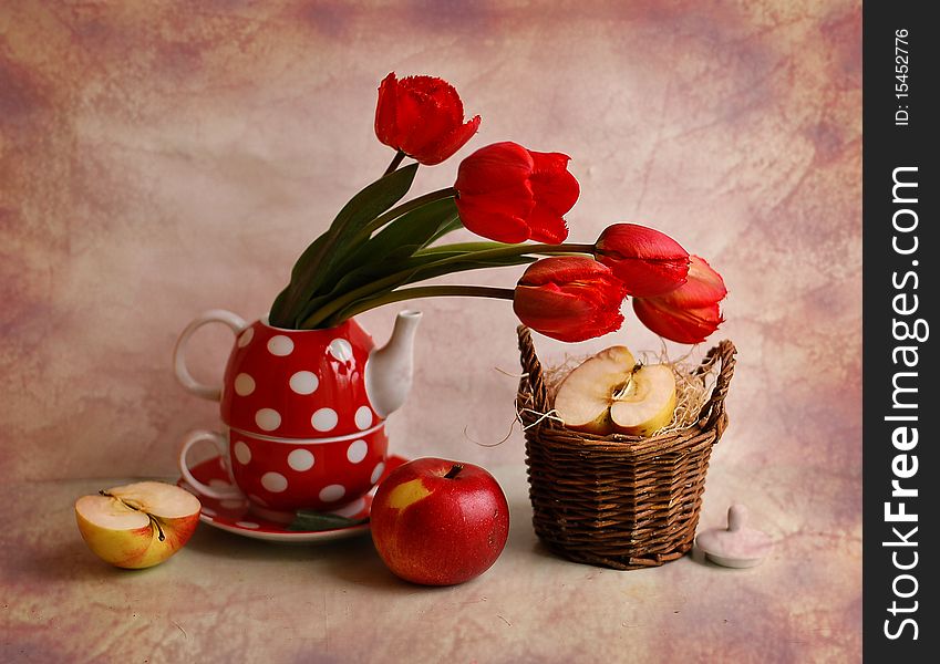 The bouquet of tulips stands in a tea-pot, alongside small basket and apples. The bouquet of tulips stands in a tea-pot, alongside small basket and apples