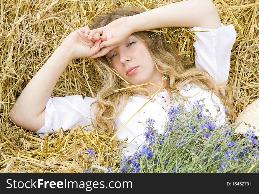 Woman lays on straw with a bunch of flowers in the summer and only has woken up. Woman lays on straw with a bunch of flowers in the summer and only has woken up