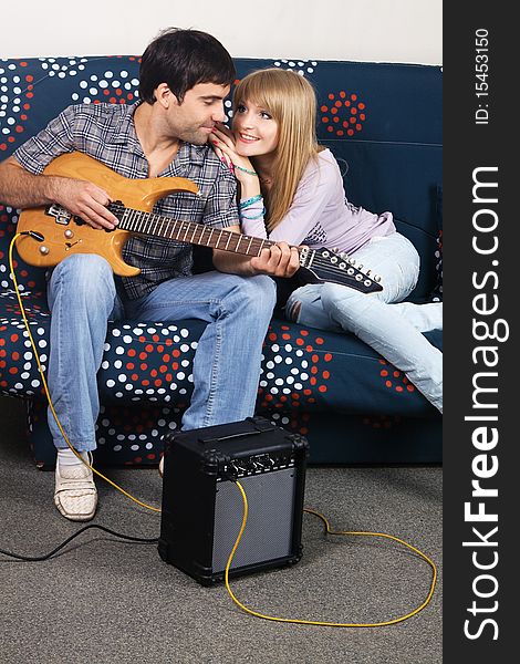 Cheerful couple resting on a sofa with electric guitar. Cheerful couple resting on a sofa with electric guitar