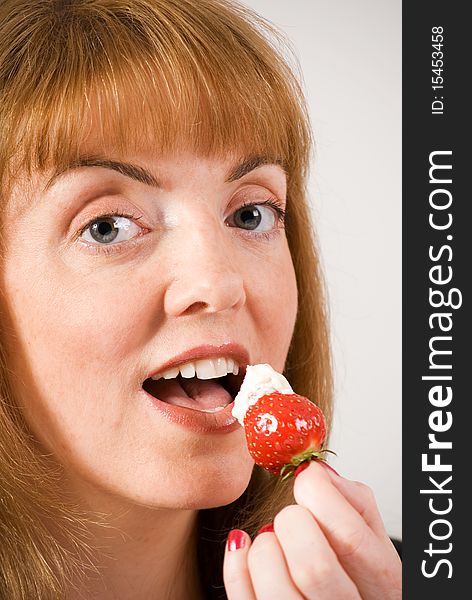 A vertical image of a pretty young woman about to eat a fresh strawberry topped with cream. A vertical image of a pretty young woman about to eat a fresh strawberry topped with cream