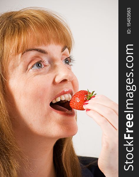 A vertical image of a pretty young woman eating a fresh strawberry. A vertical image of a pretty young woman eating a fresh strawberry