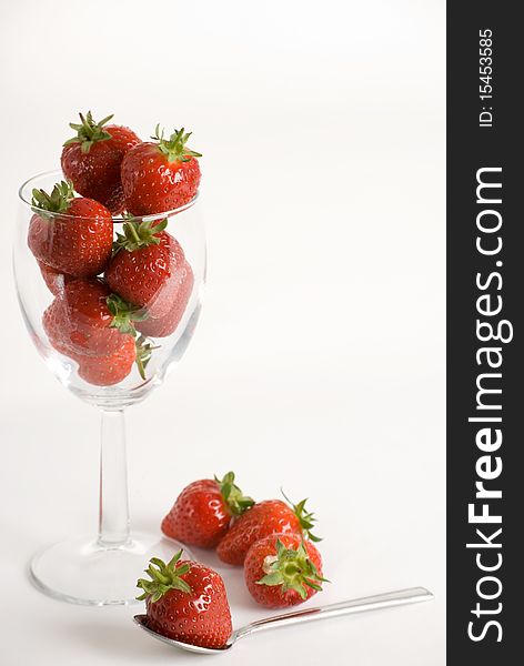 A vertical image of a wine glass filled with fresh strawberries and a spoon with one strawberry on top. A vertical image of a wine glass filled with fresh strawberries and a spoon with one strawberry on top