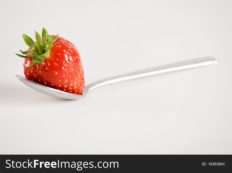 a horizontal image of a fresh strawberry on a spoon. a horizontal image of a fresh strawberry on a spoon