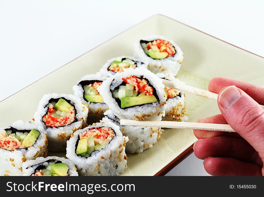 A hand holding a set of chop sticks with sushi. A hand holding a set of chop sticks with sushi.