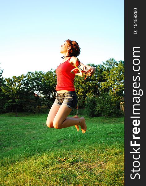 Happy woman jumping on grass wearing red clothing