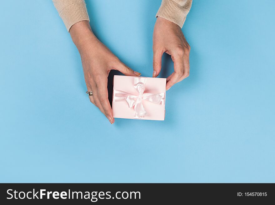 Womans hands holding gift or present box on blue pastel table top view. Flat lay  for birthday or New Year